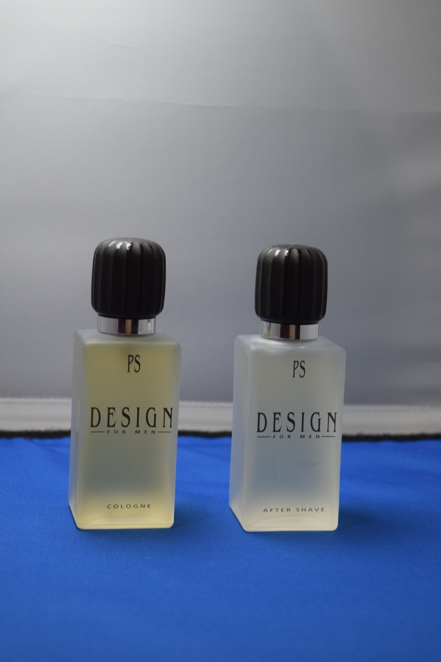 Two small bottles with black caps labeled 'PS DESIGN' on a reflective surface.