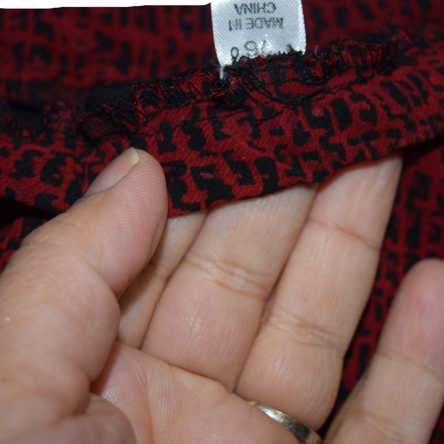 Red patterned fabric with a visible label held by a hand against a blue background