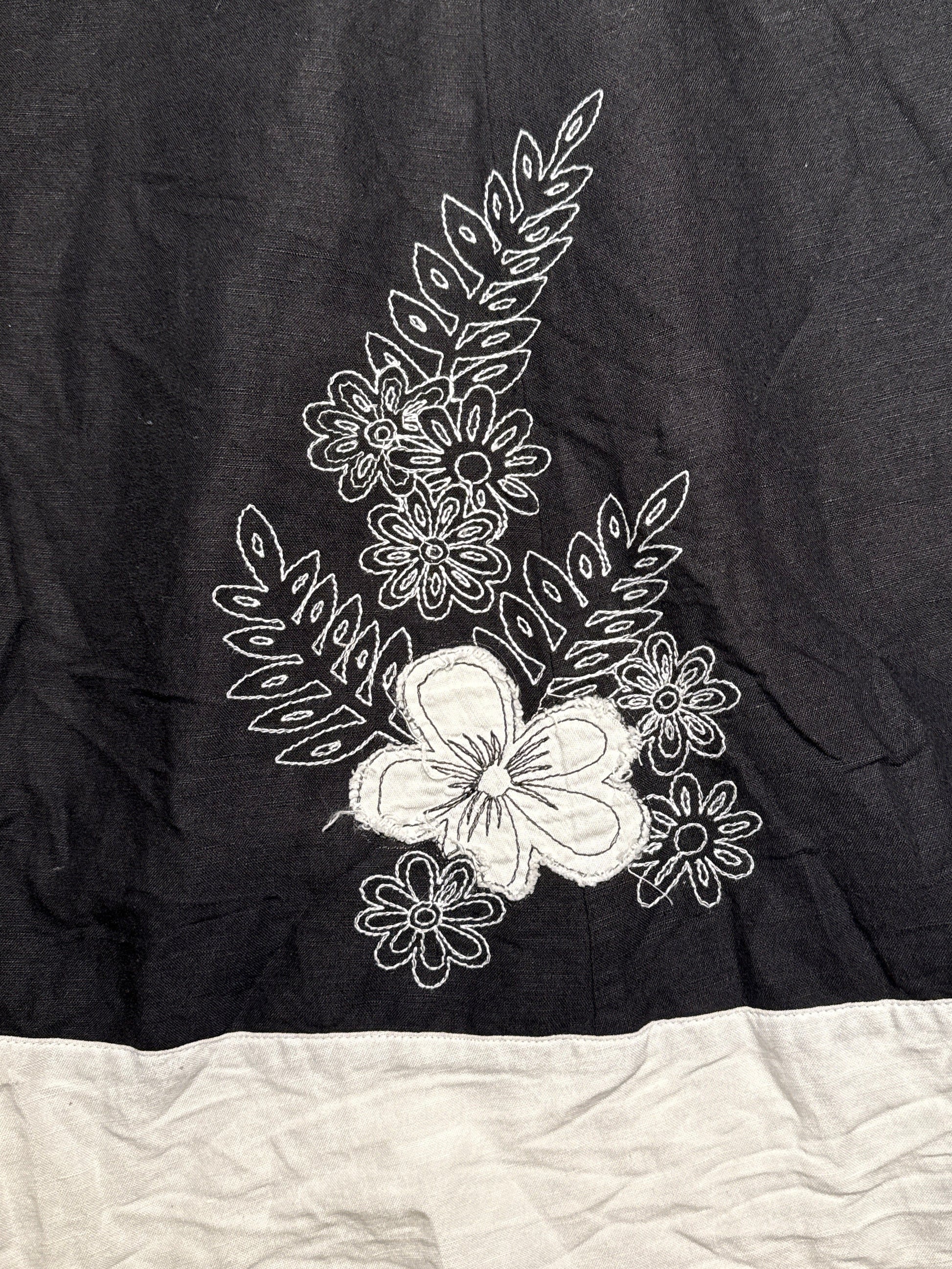 Black fabric with white floral embroidery on a beige surface